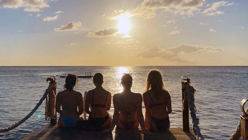 Vier junge Frauen sitzen an der Spitze des Stegs und beobachten den Sonnenuntergang am Kokomo Beach