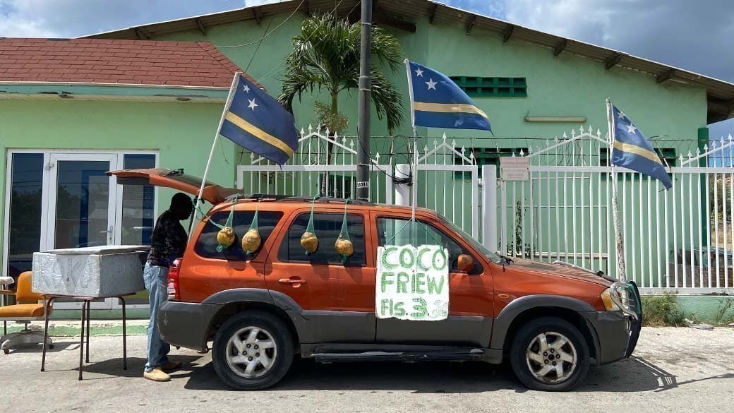 Coco friew, eisgekühlte Kokosnuss, wird auf Curacao oft und gerne am Straßenrand direkt aus dem mit Nationalflagge bestückten Auto verkauft