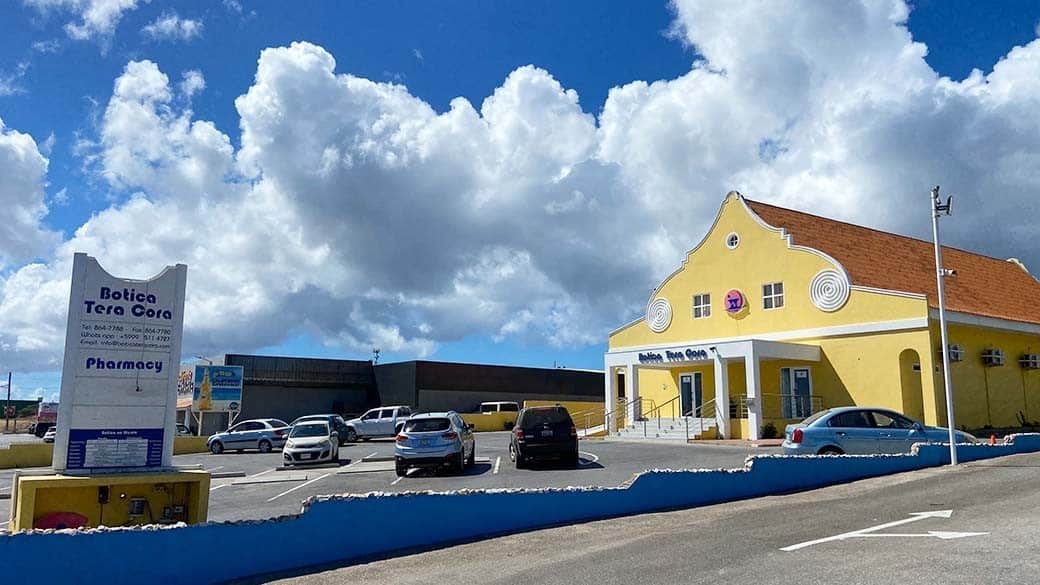 Apotheke Botica Tera Cora mit Parkplatz auf Curacao - ein gelbes Gebäude mit dem Erkennungssymbol Mörser mit Pistill